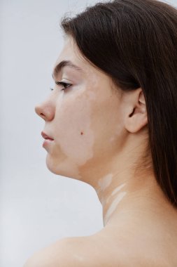 Stüdyoda beyaz arkaplana karşı poz veren güzel esmer kadının dikey profil çekimi stüdyoda doğal cilt güzelliğini kucaklıyor.