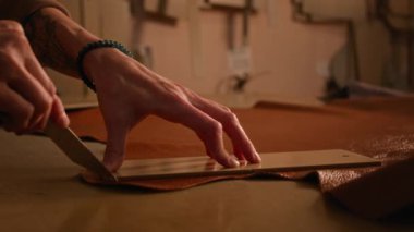 Deve derisinin üzerinde ahşap bir şablonun etrafında daireler çizen tanınmaz hale gelmiş bir el sanatları şaheseri. Loş ışıklı stüdyodaki tezgahta özel kesme aletini kullanarak.