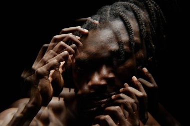 Yüzünde elleri olan siyahi bir adamın, stüdyo ortamında yüzünü kaplayan gölgelerle kameraya bakarken çift pozlama efektiyle çarpıtılmış görüntü.