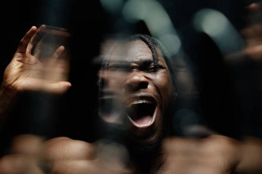 Çaresiz siyah adamın portresi yükselmiş elleriyle bağırıyor bastırılmış duyguların patlamasını yaşıyor, karanlık stüdyoda akan suyla zıt ışıkla yakalanmış.