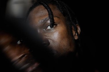 Afrika kökenli Amerikalı bir adamın tek gözü ve kamerasıyla yüzünün yarısını karanlıkta saklaması, çift çekim etkisi, kopyalama alanı.