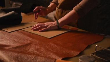 Deneyimli bronzlaştırıcının el yapımı deri çanta tasarladığı, profesyonel atölyede dikdörtgen deve derisi kestiği yüksek açılı bir çekim.