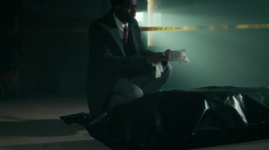 Genç siyahi adli tıp uzmanının, plastik torba altında eldiven taktığı ve kapı aralığından gelen gizemli ışıkla aydınlatılmış ıssız bir binada kanıt tabelasının yakınındaki bir yere.