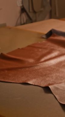 Tanınmayan tabakçının dikey yan görüntüsü, loş ışıklandırmalı profesyonel atölyede çalışan deve derisi üretimi için seçilen deve deseni.