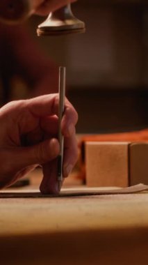 Küçük ölçekli geleneksel el yapımı stüdyoda deri işi yapan, yumruk aleti kullanan, tanınmaz hale getirilmiş, dikey çekim.