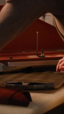 Dikey yan görünüm, tanınmayan tabakçının görüntüsü. Deri detaylarını keserken loş ışıklı atölyede duran özel basın mensuplarını kullanarak.