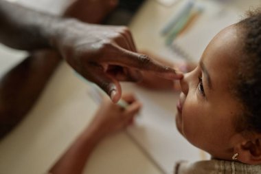Babasının küçük burnuna dokunarak kızına sevgisini ve sevgisini ifade eden küçük bir kızın evde okuduğu, boşluğu kopyaladığı görüntüsü.