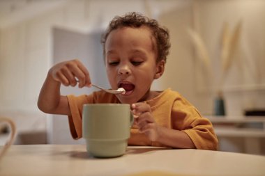 Sevimli zenci çocuğun portresi, lezzetli çikolata içeceklerinin tadını çıkarırken kaşıkla tatlı marshmallow yerken mutfakta oturup, uzayın fotokopisini çekiyor.