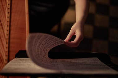 Üst görüntüde bayan arp çalgıcısının notalarla nota sayfasını çevirmesi düşük tuşlu odada müzik yaparken, boşluğu kopyala