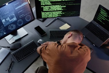 Masaüstünde yatan yorgun erkek programcının üst görüntüsü kurumsal ofisteki aşırı çalışmadan dolayı dinlenen birkaç bilgisayarla