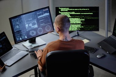 İş yerindeki erkek bilgisayar programcısının ofiste çalışırken birden fazla ekrana baktığı arka görünüm