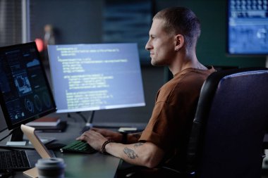 İş yerinde bilgisayar klavyesine yazı yazan yakışıklı erkek bilişim programcısının akşam saatlerinde şirket ofisinde kod yazışının yan görüntüsü