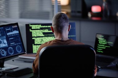 Ofiste akşam saatlerinde çalışan birçok bilgisayar ekranı yazma programıyla birlikte masadaki erkek bilişim geliştiricisinin arka görünümü
