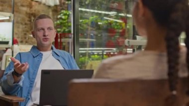 Önündeki bayan meslektaşıyla birlikte dizüstü bilgisayarla koltukta oturmuş dikey çiftçiliği tartışan beyaz bir adamın orta omuzundan vuruşu.