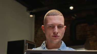 Laptop 'un önünde iç mekanlı kahve dükkanında günlük giysiler içinde çalışan genç beyaz adamın yakın plan fotoğrafı.