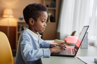 Orta boy siyah çocuğun dizüstü bilgisayarda yazı yazarken, ödev yaparken ya da yatak odasındaki pencerenin yanındaki masada otururken video oyunu oynarken, boşluk kopyalarken.