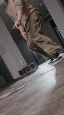 Dikey çekimde yetenekli beyaz erkek zoomer dans salonunda hip hop müzik eşliğinde rock ve güç hareketleri yaparak gücünü ve yaratıcılığını gösteriyor.