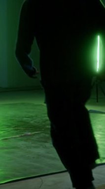 Dikey geniş açı, genç yetenekli beyaz break dans yapan, mükemmel ayak hareketlerini ve yaratıcılığını gösteren, yeşil ortam ışığı altında kapalı alanda pratik yapan