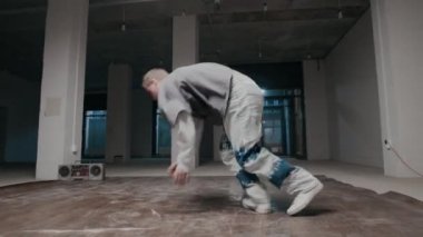 El kamerasıyla, kapalı alanda break dans yaparken hip hop kıyafetleri giyen yetenekli beyaz çocuk tek eliyle dondurucu hareketler yapıyor.