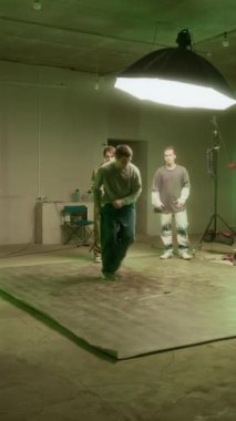 Sokak kıyafetleriyle beyaz erkek zoomer 'ın dikey çekimi onu destekleyen akranların önünde break dans ve hip hop müziği eşliğinde dans ederken.