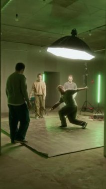 Kentsel giyim kuşağında beyaz Z gençlerinin dans pistinin ortasında dans eden genç adamı izlediği, onu desteklediği ve hip hop havasından keyif aldığı dikey geniş bir görüntü.