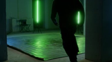 Geniş açılı yetenekli beyaz break dans yapan harika ayak hareketlerini ve yaratıcılığını gösteren yeşil ışık altında kapalı alanda pratik yapan çocuk.