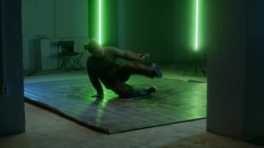 Yavaş, yetenekli, beyaz bir adam enerji ve bireysellik dolu kaya hareketleri sergiliyor, yeşil neon ışığın altında kapalı alanda pratik yapıyor.