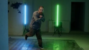 Sokak elbiseli beyaz tenli bir gencin en iyi rock 'ı pratik yaparken, kapalı alanda yeşil ve mavi lambaların altında break dans yaparken görüntüsünü yakınlaştırıyorum.