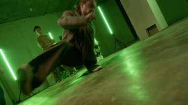 Sokak giysili beyaz bir adamın yeşil ışık altında evin içinde erkek zoomerların önünde kırılışının zemin katındaki çekimi.