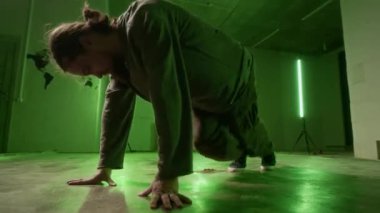 Sokak giysisinde el ve ayaklarla dans ederken zemin katta yeşil neon ışığın altında kaya hareketleri çalışırken.