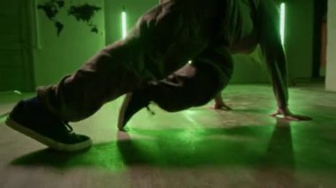 Kentsel giyimli bir adamın yeşil neon ışığın altında pratik yapıp ayak becerilerini geliştirdiği el kamerası görüntüsü.