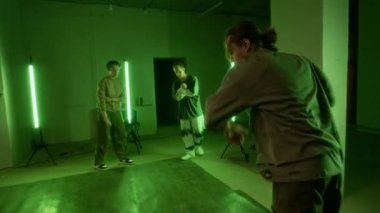 Breakdance savaşına katılan genç ve yetenekli beyazın el kamerasıyla çekilmiş bir fotoğrafı. Dans salonundaki genç meslektaşlarının önünde havalı hareketler yapıyor. Yeşil neon ışığıyla aydınlatılıyor.