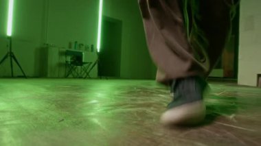 Şehir kıyafetli, yeşil lambalarla break dansın en iyi hareketlerini pratik yapan isimsiz bir adamın bacaklarının yavaş çekimleri.