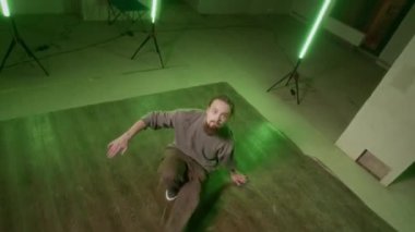Sokak kıyafetleri içindeki beyaz bir gencin canlı yeşil ışık altında dans ederken kameraya baktığı yüksek açılı bir çekim.