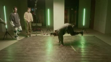 Sokak kıyafetleri içinde beyaz sakallı genç bir adam müzik kutusundaki breakdance numaralarını gösteriyor ve beyaz Z jenerasyonundaki çocuklar onu izliyorlar.