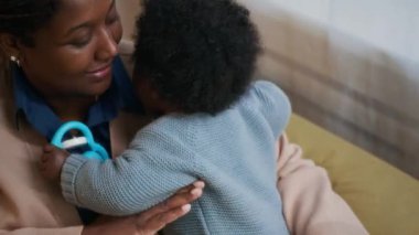 Afrika kökenli Amerikalı bir annenin, bebeğine sarılıp öptüğü, rahat bir dairede kanepede oynadığı yüksek açılı bir fotoğraf.