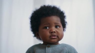 Beyaz arka planda sakin bir ifadeyle kameraya bakan kıvırcık saçlı sevimli Afrikalı Amerikalı çocuğun yakın plan portresi.