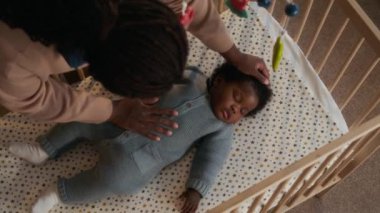 Afro-Amerikan annenin, beşikte uyurken bebeğinin saçlarını dikkatle okşamasının en iyi görüntüsü.