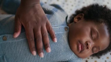 Tanımlanamayan Afro-Amerikan annenin yakın planda çekilmiş fotoğrafı. Onu okşarken, şablonlu bir bebeğin üzerinde uyuyor.