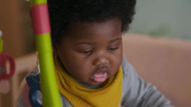 Sarı önlüklü, kıvırcık saçlı Afrikalı Amerikalı çocuğun bebek odasına baktığı yakın plan bir fotoğraf.