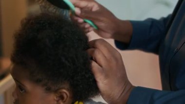 Afro-Amerikan bebeğinin, tanınmayan annesinin kıvırcık saçlarını morarttığı sırada sabırsız olduğu yakın plan çekimleri.