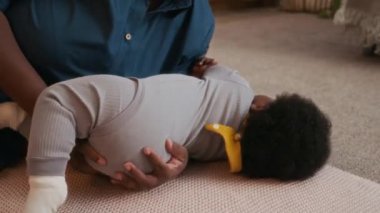 Afrika kökenli Amerikalı anne bebeğini nazikçe kucaklıyor ve okşuyor, halı döşeli yerde uzanıyor ve eğleniyor.