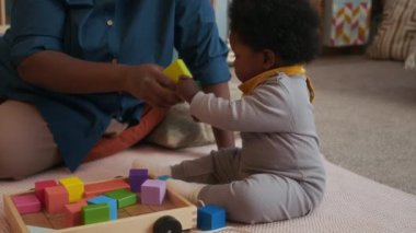 Yavaş çekimde gülümseyen anne bebeğiyle vakit geçiriyor oyuncaklarla oynuyor, çocuk odasında yerde oturuyor.