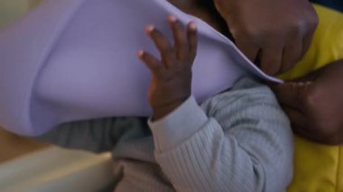 Tanımlanamayan Afrikalı Amerikalı annenin bebeğine önlük giydirip öğle yemeğinden önce yüksek sandalyede oturduğu yakın çekim.