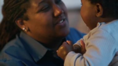 Neşeli ve sevecen Afrikalı Amerikalı annenin bebeğini kucağına alıp onunla konuştuğu yakın çekim.