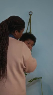 Şefkatli Afrikalı Amerikalı annenin bebeğini kucağında tutarken ve onu bebek odasında yatırırken dikey pozu.