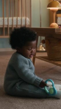 Dikey çekimde, Afrikalı Amerikalı çocuk bebek bebek halı döşeme üzerinde oturuyor ve çıngıraklı oyuncakla tek başına oynuyor.
