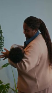 Afrika kökenli Amerikalı bir annenin bebeğini kucağında sallarken, rahat bir bebek odasında kollarında uyuduğu dikey bir fotoğraf.