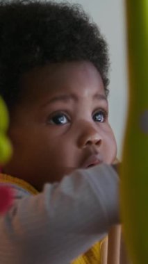 Kıvırcık saçlı ve beşiğine yaslanmaktan kafasını kaldırıp bakan sevimli Afrikalı Amerikalı çocuğun dikey yakın çekimi.