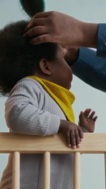 Tatlı Afro-Amerikan bebeğinin, tanınmayan annesinin saçını yaparken sabırlı olduğu dikey yavaş çekim.